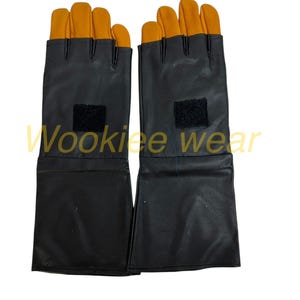 Pu&ograve; includere: Un paio di guanti neri con le punte delle dita arancioni. I guanti hanno un polsino lungo e una toppa in velcro sul dorso della mano. Il testo "Wookiee wear" &egrave; visibile nell'immagine.