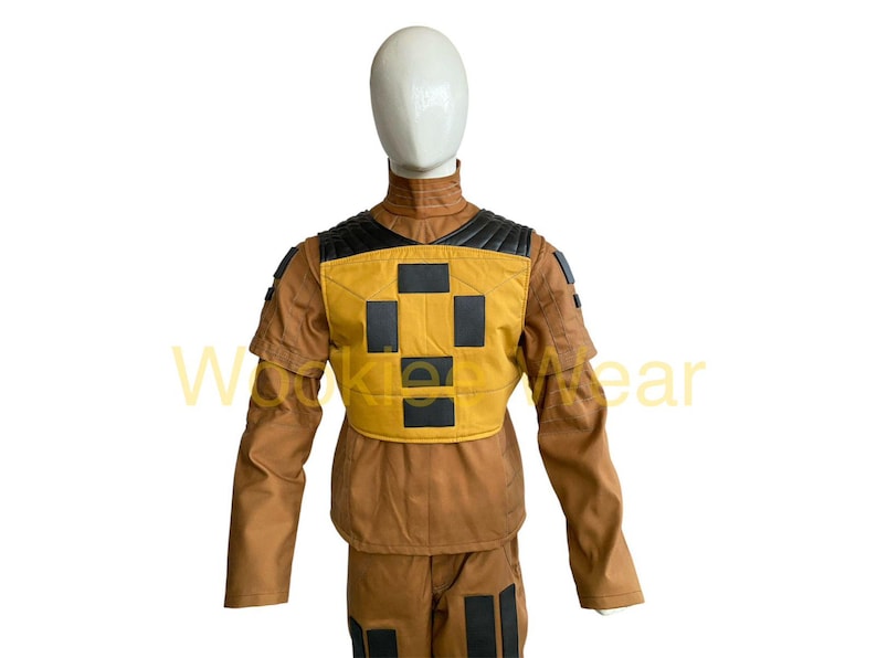 May include: A brown and yellow jumpsuit with black accents, displayed on a mannequin. The outfit features a yellow chest panel with a black cross design and black shoulder detailing. The sleeves and pants have black rectangular details.