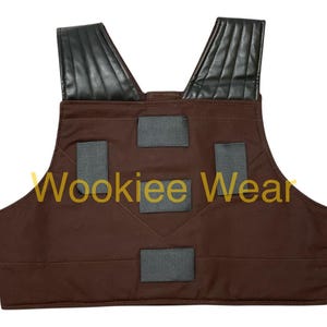 May include: Brown vest with black shoulder pads and gray rectangular accents. The text "Wookiee Wear" is printed in gold across the front. The vest is designed with a V-neck and is likely part of a costume.