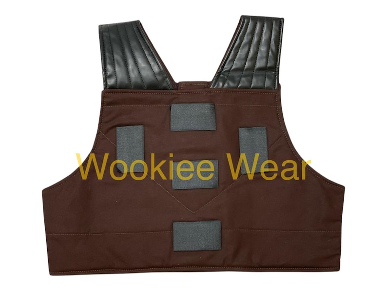 May include: Brown vest with black shoulder pads and gray rectangular accents. The text "Wookiee Wear" is printed in gold across the front. The vest is designed with a V-neck and is likely part of a costume.