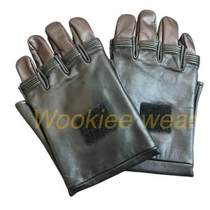 Pu&ograve; includere: Un paio di guanti neri senza dita con punte delle dita e dei pollici marroni. I guanti hanno una piccola toppa quadrata nera sul polso e il testo "Wookiee wear" &egrave; visibile sul guanto sinistro.
