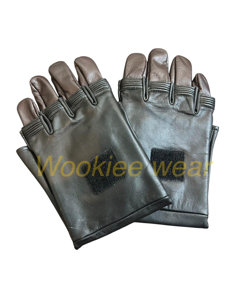 Pu&ograve; includere: Un paio di guanti neri senza dita con punte delle dita e dei pollici marroni. I guanti hanno una piccola toppa quadrata nera sul polso e il testo "Wookiee wear" &egrave; visibile sul guanto sinistro.