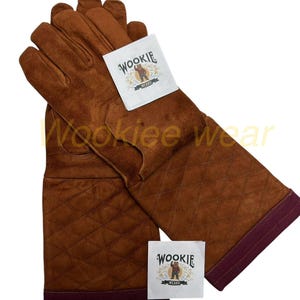May include: Brown leather gloves with a quilted pattern on the gauntlets. The gloves have a dark burgundy trim at the cuffs and a white tag with the text "Wookiee Wears" and a bear logo.