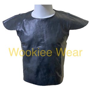 Puede incluir: Una camiseta sin mangas de color gris oscuro con mangas cortas, exhibida en una cabeza y torso de maniquí blancos. La camiseta tiene un cuello redondo y está hecha de un material texturizado. El texto "Wookiee Wear" es visible en amarillo.