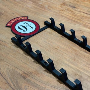 Peut inclure: Porte-manteau mural en métal noir avec plusieurs crochets. Comprend une enseigne circulaire avec le texte "PLATFORM" et "9 3/4" en rouge, blanc et noir. Le porte-manteau est conçu pour suspendre des objets.