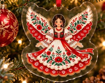 May include: A clear acrylic Christmas ornament shaped like an angel with brown hair, wearing a white dress featuring red and green floral patterns. The angel has large wings decorated with red poppies and green leaves, suspended by a red ribbon.