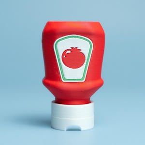 Puede incluir: Una botella de ketchup roja con una base blanca y una etiqueta verde y blanca con una ilustración de tomate. La botella está centrada sobre un fondo azul claro.