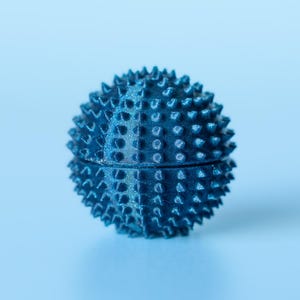 May include: A blue spiky ball, similar to a sea urchin, sits against a light blue backdrop. The ball's surface is covered in evenly spaced, conical spikes. The object is spherical, and the colour is a deep, saturated blue.
