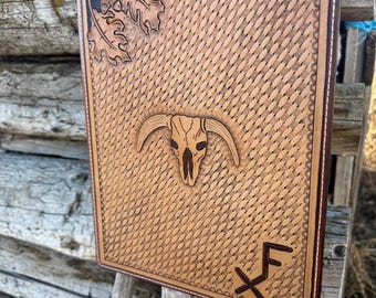 Puede incluir: Un cuadro de pared rectangular de cuero marrón claro con un diseño tallado. El diseño incluye una calavera de toro, hojas de roble y las letras "XF". El borde es marrón oscuro con costuras blancas.