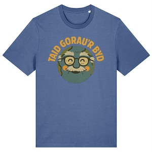 May include: Blue t-shirt featuring a cartoon illustration of a smiling face with glasses, a mustache, and the text "TAID GORAU'R BYD" in orange. The graphic is centered on the front of the shirt.