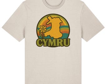 May include: A light beige t-shirt featuring a retro design with the word "CYMRU" in green block letters. The design includes a yellow outline of Wales, a daffodil, and a rainbow-colored background.