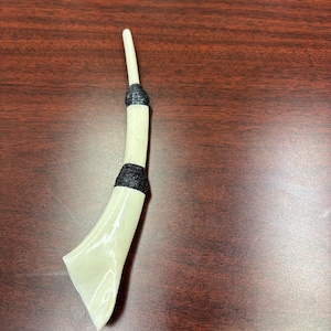 May include: A cream-colored, elongated object with a flared end, wrapped with black material at two points. The object has a smooth, glossy finish and a slender, straight top.