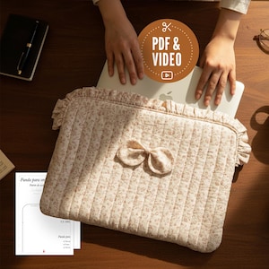 Puede incluir: Una funda para portátil beige con estampado floral y lazo. La tela acolchada presenta un diseño floral rosa y un borde con volantes. El texto "PDF & VIDEO" está en un círculo marrón. Un portátil está dentro.