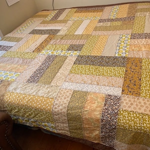May include: A patchwork quilt with a variety of brown, beige, and green floral patterns. The quilt is made of different fabric scraps sewn together to create a unique design.