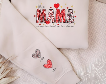 May include: Beige sweatshirt and sleeve set with the text "This MAMA wears her heart on her sleeve." The word "MAMA" is decorated with hearts and leopard print. The sleeve has two heart designs with names.