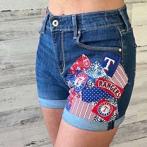 May include: Blue denim shorts with a patchwork design featuring red, white, and blue fabric scraps. The patches include the words "Texas Rangers" and a baseball logo.
