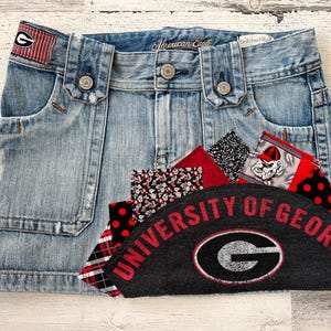 Puede incluir: Una falda vaquera con parches, incluyendo un parche de la Universidad de Georgia, cuadros rojos y negros, lunares rojos y blancos y un estampado floral rojo y blanco.