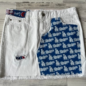 Könnte beinhalten: Weißer Jeansrock mit einem blauen und weißen Stoffpanel mit dem wiederholten Text "LA Dodgers". Der Rock hat einen ausgefransten Saum und ein Destroyed-Detail auf der Vorderseite.