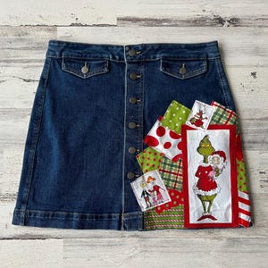 May include: A blue denim skirt with a button-up front and a patchwork design. The patchwork includes red, green, and white fabric with a cartoon character of the Grinch holding a Christmas present.