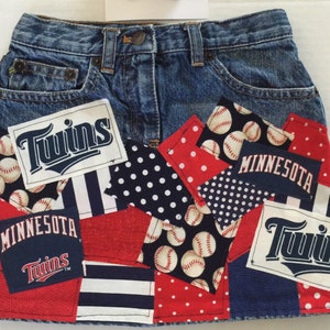May include: A denim skirt with patches of red, white, and blue fabric. The patches feature baseballs, polka dots, and the words "Twins" and "Minnesota".