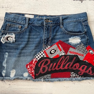 May include: A denim skirt with a patchwork design featuring red, black, and white fabric. The patchwork includes the word "Bulldogs" and a University of Georgia logo.