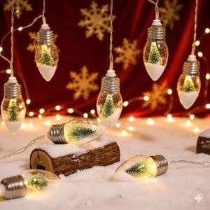 Op de afbeelding: Slinger van kerstverlichting met heldere, bolvormige ornamenten. Elk ornament bevat een kleine groene kerstboom en witte sneeuw. De lampjes zijn geregen aan een dun draadje, met een warme, gele gloed. De achtergrond is dieprood met gouden sneeuwvlokversieringen.