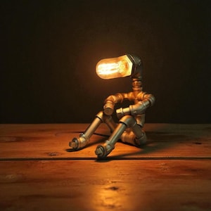 May include: A unique, industrial-style desk lamp shaped like a person sitting with their legs crossed. The lamp is constructed from metal pipes and fittings, with a lightbulb as the head. The warm light from the bulb illuminates the surrounding area, creating a cozy ambiance.