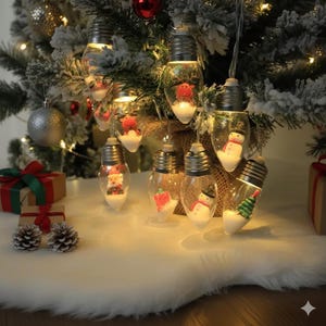 May include: A string of clear light bulbs with silver bases, each containing a miniature Christmas figure. The figures include Santa Claus, snowmen, reindeer, and Christmas trees. The lights are strung on a wire and are displayed on a Christmas tree.
