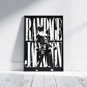 Peut inclure: Impression encadrée en noir et blanc représentant un combattant musclé. Le nom "Rampage Jackson" est affiché en grandes lettres blanches. Le combattant est en position de combat, portant un short et des gants. L'impression est posée contre un mur blanc sur un sol en bois.
