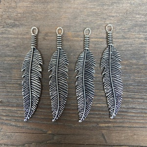 May include: Four silver feather charms with a detailed design. The charms have a loop at the top for attaching to jewelry or other crafts.