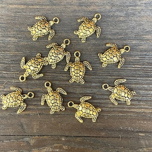 May include: Ten gold-colored turtle charms with a detailed design. The charms have a loop at the top for attaching to jewelry or other crafts.