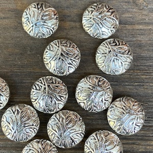 May include: A collection of silver-toned metal buttons with a tree branch design. The buttons are round and have a raised design.