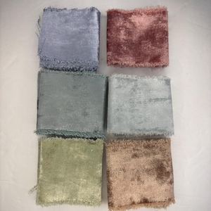 May include: A collection of six velvet ribbon swatches in various colors. The colors include light blue, dusty rose, gray-green, light blue-gray, pale green, and a muted brown. Each swatch has a frayed edge.