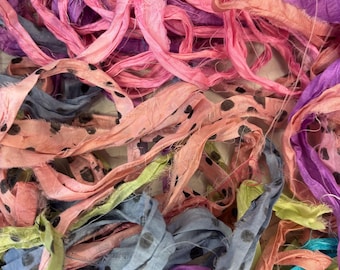 Könnte beinhalten: Nahaufnahme von bunten Stoffstreifen in Rosa, Lila, Blau und Gelb. Einige Streifen haben schwarze Tupfen. Der Stoff scheint Seide oder ein ähnliches Material zu sein, mit einer leicht ausgefransten Textur. Ideal für Bastel- oder Textilprojekte.