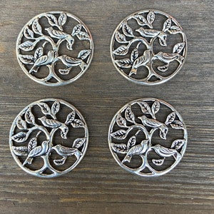 May include: Four silver metal round ornaments with a tree and birds design. Each ornament features a stylized tree with branches and leaves, and three birds perched on the branches.