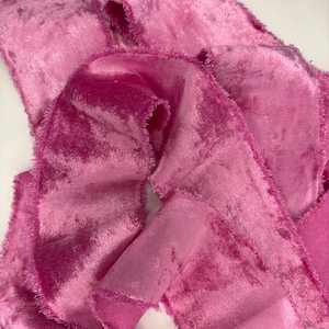 May include: Close-up of pink velvet ribbon with frayed edges. The ribbon is a vibrant shade of pink, with a soft, textured appearance. The fabric is folded and layered, creating a sense of depth and dimension. Ideal for crafting and decorative projects.