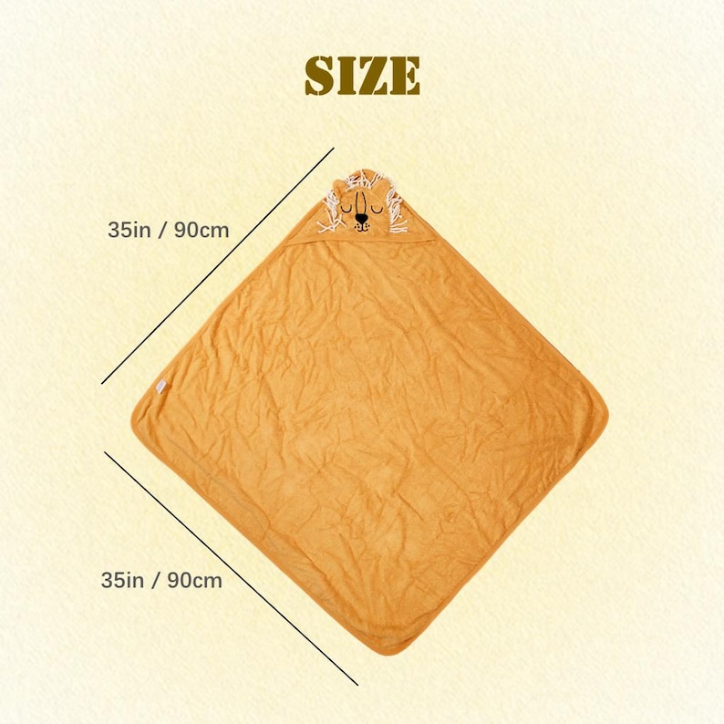 Puede incluir: Una toalla con capucha amarilla mostaza para beb&eacute; con una cara de le&oacute;n bordada en la capucha. La toalla mide 90 cm por cada lado. La palabra "SIZE" est&aacute; impresa en la parte superior de la imagen.