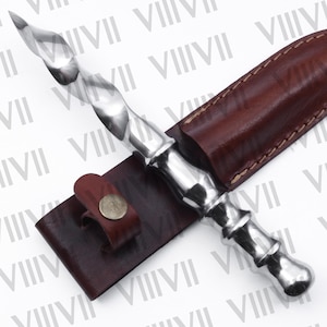May include: A silver dagger with a twisted blade and a brown leather sheath. The dagger has a decorative handle and is secured in a sheath with a leather strap and a metal button.