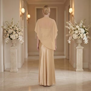 This graceful ivory silk dress features a soft cowl neckline and a detachable sheer cape, making it an elegant choice for formal bridal events. With its flowing silhouette and asymmetrical cape hem, it’s perfect for bridesmaids, wedding guests, or even as a luxurious bridal shower gift. The timeless design and refined look make it a fantastic option for those searching for a thoughtful, sophisticated gift for any wedding celebration.
