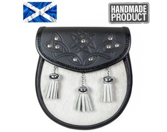 May include: A sporran featuring a white fur front panel with three white leather tassels hanging from silver-toned chains. The black leather flap is embossed with intricate Celtic knotwork and accented with silver-toned metal studs.