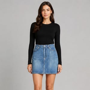 Puede incluir: Una camiseta negra de manga larga con cuello redondo combinada con una minifalda de mezclilla azul. La falda presenta un diseño clásico de cinco bolsillos, cierre de botón y cremallera, y costuras visibles en un acabado de lavado medio.