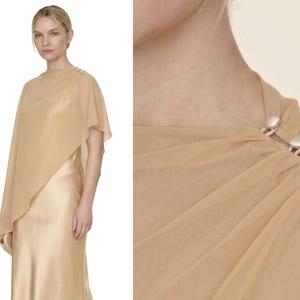 This stunning soft champagne silk dress with a detachable sheer cape combines elegance with a contemporary edge, perfect for a wedding or bridal event. The cowl neckline and asymmetrical cape hem add movement and grace, making it a fantastic option for bridesmaids, wedding guests, or as a luxurious bridal shower gift. It’s ideal for gifting during bridal celebrations, offering a polished yet understated way to celebrate the occasion.