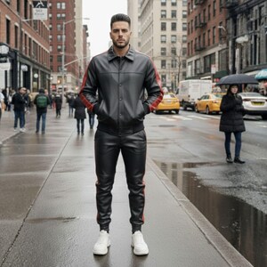 May include: Black leather jacket and matching pants with red stripes on the sleeves and legs. The jacket has a button-up front and pockets. The outfit is paired with white sneakers. The person is standing on a wet city street.