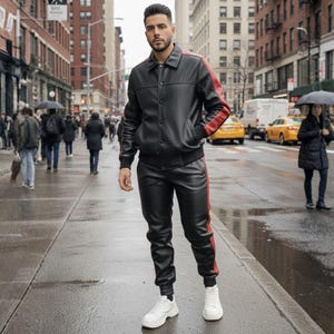 May include: A person wearing a black leather jacket with red stripes on the sleeves and matching black leather pants with red stripes. The person is wearing white sneakers and standing on a wet sidewalk in a city.