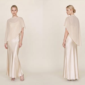This ivory silk gown with a detachable sheer cape is the epitome of bridal elegance. Featuring a flattering cowl neckline and asymmetrical cape hem, it makes a stunning addition to any formal occasion, from weddings to bridal showers. Ideal as a bridal gift or a bridesmaid dress, this gown embodies sophistication and timeless charm, making it the perfect choice for those looking for an exquisite bridal party outfit or a thoughtful fashion gift.