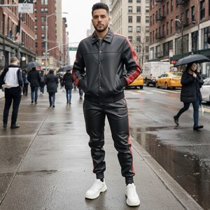 May include: A black leather jacket and matching pants with red stripes. The jacket has a button-up front and the pants have a drawstring waist. The person is wearing white sneakers. The background is a city street with people and cars.