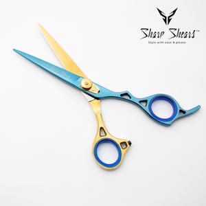 以下が含まれることがあります： 金色の刃と青色のハンドルが付いたプロ仕様のヘアシザー。シザーには金色のピボットネジと青色の指輪が付いています。「Sharp Shears」の文字がシザーに印刷されています。