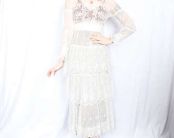 May include: A white lace dress with a tiered skirt and long sleeves. The dress has a fitted bodice and a delicate floral pattern. The model is wearing the dress with green shoes.