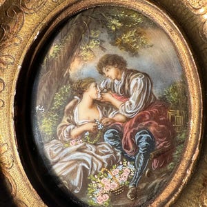 Può includere: Dipinto ovale antico in una cornice dorata ornata. Il dipinto raffigura una coppia in un giardino, con l'uomo che offre un fiore alla donna. L'opera presenta colori tenui e un tema romantico, con una firma nell'angolo.