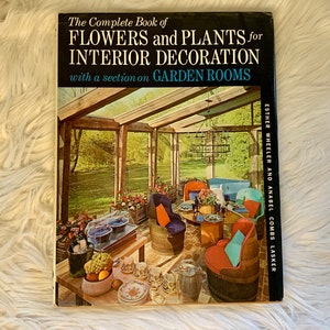 May include: The Complete Book of Flowers and Plants for Interior Decoration with a section on Garden Rooms by Esther Wheeler and Anabel Combs Lasker. The book cover features a photo of a sunroom with a table set for a meal, surrounded by chairs and plants.